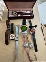 Photo showing eight character-themed watches arranged on table including boxed Cinderella watch with brown leather band, various bands in pink, beige, black, light blue, and character designs.