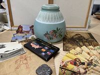 Photo of assorted items including blue ceramic or glass lamp shade with floral design, small tin or box with flag pins, paper fan with colorful illustrations, vintage postcards, and antique metal opener.