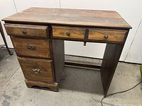 Photo shows the full farmhouse style wooden desk with visible wood grain finish consisting of three stacked drawers on the left side and one long shallow drawer in the center.