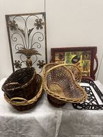 Photo showing metal floral wall decor with pineapple motif, three wicker baskets, colorful breakfast tray, and cast iron casserole caddy