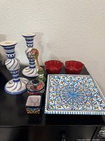 Photo showing pair of tall white and blue spiral ceramic candlesticks, two fluted red ceramic bowls, a blue and white Italian ceramic catch-all tray, Mexican ceramic bowl and planter, and small colorful spoon and holder.
