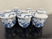 Photo showing six Japanese porcelain teacups with lids with blue lotus flower and leaf design from the side.