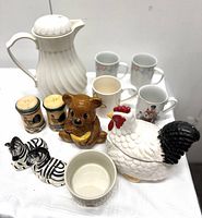 White ribbed ceramic carafe with lid, ceramic chicken bowl with black tail, honey bear pot, zebra and rooster salt and pepper shakers, four ceramic mugs, and ceramic bowl.
