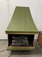 Front view of an olive green Midcentury Modern electric fireplace with brass trim, displaying faux fire logs and metal mesh screen in front.