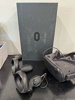 View of Oculus Quest black VR headset, two black wireless controllers, and partial black box with Oculus logo