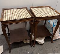 Two vintage solid wood parlor tables side by side with tiled tops and claw and ball feet.
