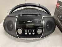 Front view of the RCA portable CD player showing the speakers, control buttons, display screen, and handle on top.
