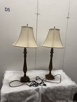 Pair of tall vintage Quoizel table lamps with beige fabric shades, shown front view with cords coiled in front.