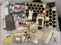Top-down view of assorted sewing notions spread on a surface including bobbins, needles, lace, thread spools, tapes, and tools.
