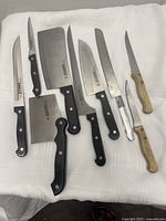 Top view of 7 cutters and knives including Showtime branded with black handles, and 3 wooden handled pieces.
