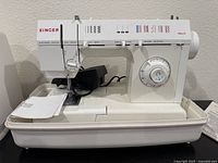 Full front view of Singer 5830C sewing machine inside hard white carrying case showing stitch selection and machine controls.