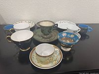 Top view showing 8 cups and saucers with various patterns, colors including black, green, blue with gold, floral
