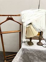 Wooden valet stand with two Quoizel brass table lamps, one with a fabric shade and one missing its shade.