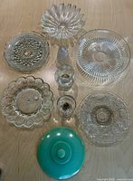 Photo showing seven clear glass items and one green Jadeite lid on wood surface.