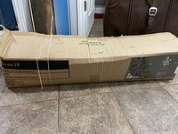 Cardboard box packaging of artificial Christmas tree showing shape and size on tiled floor