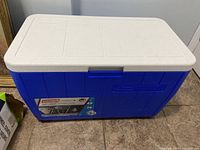 Blue Coleman cooler with white lid on tiled floor.