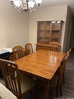 Overall view of the dining table surrounded by six chairs and showing the buffet cabinet against the wall.