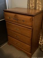 Tall wooden dresser with four drawers in a natural wood finish, metal ring pulls on top drawer, metal bar handles on other drawers, standing on bracket feet.