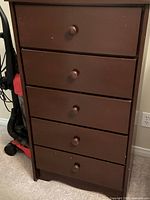 Full front view of the brown wooden tall dresser showing five drawers with round wooden knobs and minor surface wear.