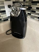 Black Hamilton Beach electric can opener on kitchen counter, viewed front right angle showing logo.