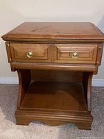 Front view of a wooden end table showing a drawer with two brass knobs and open shelf underneath