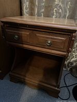 Full view of wooden end table showing top, drawer front with metal ring handle, and open bottom shelf.