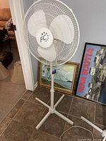 White FC brand floor standing fan shown with three translucent blades and adjustable height stand on a tiled floor.
