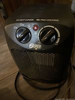 Front view of black SuperNote portable heater showing control knobs, red power light, and safety warning text on top.