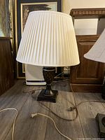 Full view of the table lamp showing the pleated white fabric shade and textured dark base on square platform on wooden floor.