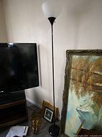 Tall floor lamp next to a TV and some framed paintings leaning against the wall.