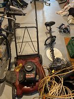 Photo showing the complete red Yard Machines 300 Series lawn mower with 148cc Briggs & Stratton engine, black push handle, and side grass chute with miscellaneous garage items around.