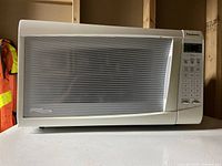 Photo of a white small Panasonic microwave oven with a digital keypad and a front window with horizontal lines on a white surface.