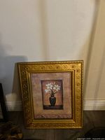 Photo of a single framed picture showing floral art in a decorative gold frame against a plain wall.