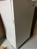 White upright freezer, angled front view showing door and handle