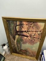 Framed painting leaning against wall, showing pink-leaved trees and a natural landscape with a path.
