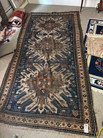 Full view of rectangular antique Caucasian Kazak rug with larger repeating eagle and flower motifs on blue background and geometric borders, placed on floor indoors.