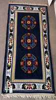 Full view of rectangular wool area rug with three central round medallions and decorative border, mainly dark blue with accents of red, white, green, and gold.