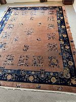 Full view of large area rug showing rust field, navy blue floral border, and fringe