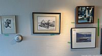 Wall display showing five framed artworks including a dragon woodcut, reproduction of two men with oxen, watercolor boat, and two abstract pieces.