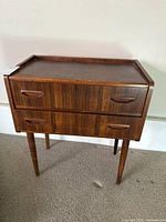 Front view of wood two-drawer side table on tapered legs with built-in handles