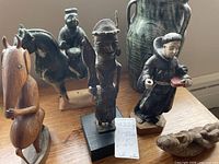 Group view: wooden anteater, ceramic horse and rider, bronze warrior, wooden monk, stone fertility figure