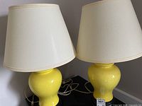 Photo of two matching yellow ceramic base lamps with white lampshades, showing overall appearance and pairing.