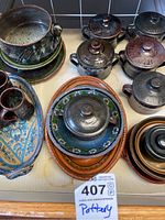 Overview of various pottery items including lidded jars, stacked bowls, cups, and colorful trays in different glazes.