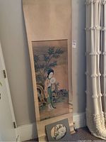 Full view of the scroll painting hanging leaning against the wall near a door and curtain.