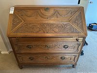 Front view of the wood secretary desk showcasing carved detail on the drop-down front and the two drawers below, with metal hardware pulls.