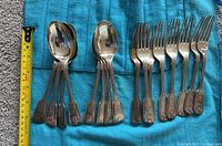 16-piece arrangement showing two stacks of eight tablespoons on left and eight forks on right against blue cloth with measuring tape