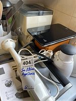 Lot of small kitchen appliances including scales, panini grill, mixer with cords