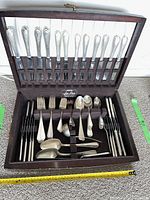 Open fitted wooden case showing top row holding twelve dinner knives with sterling silver handles and stainless blades
