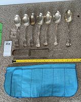 Overhead view of seven serving spoons and slide-action tongs laid side by side on carpet with measuring tape.