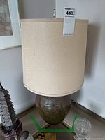 Full view of lamp showing beige drum lampshade and rounded ceramic base with carved decoration.